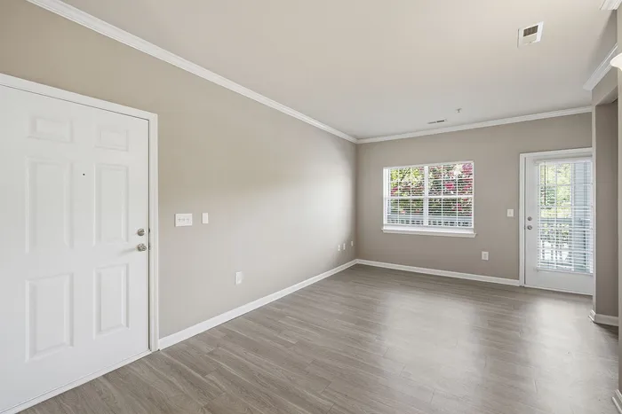 Bright and airy living space with sleek flooring, large window, and glass door leading to a serene outdoor view.