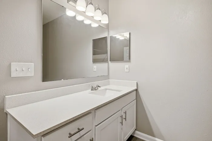 Elegant bathroom with a pristine countertop, large mirror, and modern light fixtures offering a sophisticated touch.