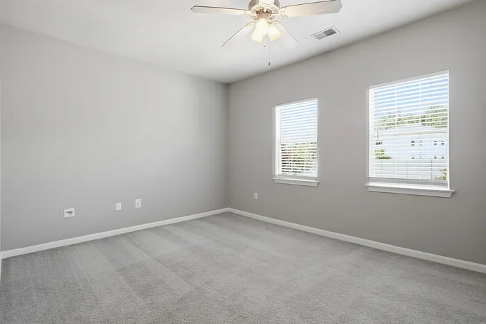 Bright, spacious bedroom with plush carpet, neutral walls, and abundant natural light from large windows.