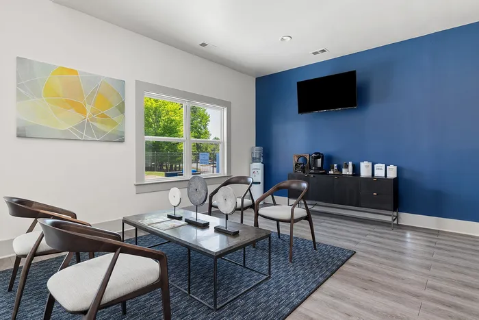 Modern communal lounge with sleek chairs, vibrant art, and a coffee station against a striking blue accent wall.