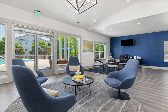 Elegant apartment lounge with modern blue chairs, stylish decor, and bright windows overlooking a serene outdoor pool area.