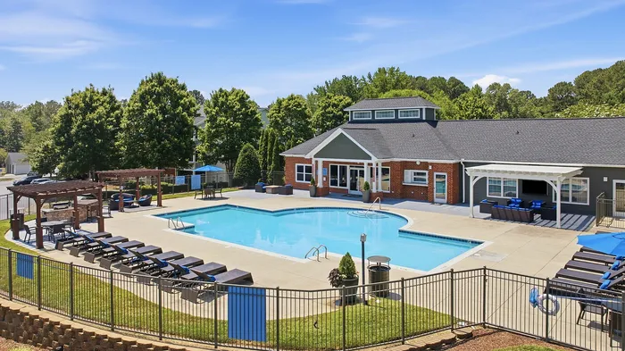 Luxurious outdoor pool area with sun loungers, pergolas, and a modern clubhouse surrounded by lush trees.
