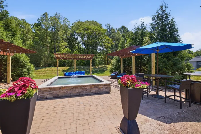 Charming outdoor patio with pergolas, vibrant flower planters, cozy seating, and a serene water feature.