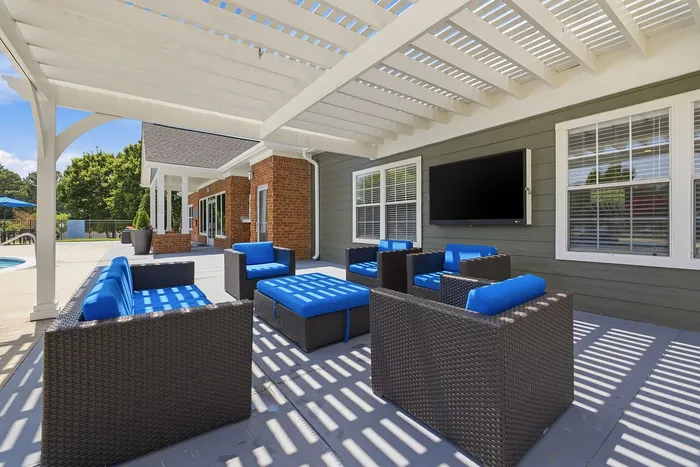Charming outdoor patio with cozy wicker seating, vibrant blue cushions, and a spacious TV area under a stylish pergola.