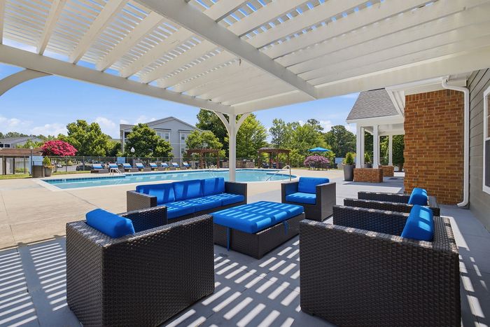 Luxurious outdoor pool area with elegant wicker furniture and vibrant blue cushions under a stylish pergola, perfect for relaxation.