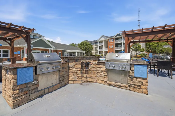 Inviting outdoor grill area with sleek barbecue stations and stonework set in a modern apartment community, perfect for social gatherings.