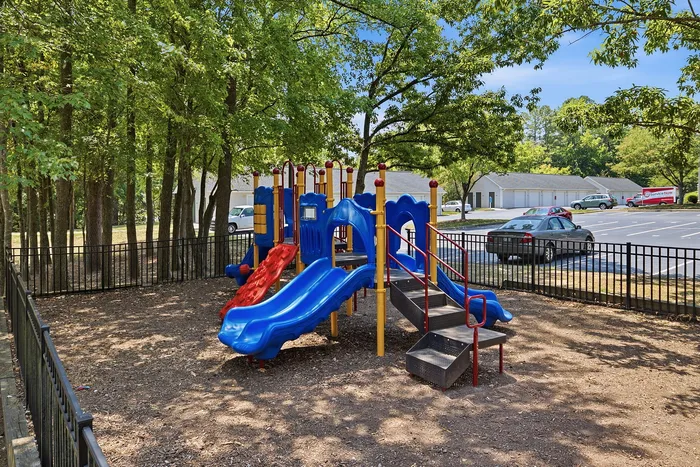 Inviting outdoor playground with vibrant slides and climbing structures, surrounded by lush trees and secure fencing, ideal for family-friendly living.