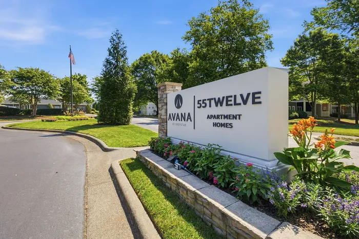 Inviting entrance of 55Twelve Apartment Homes surrounded by lush greenery and vibrant flowers.