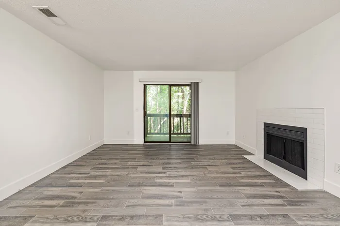Elegant living room with modern wood flooring, a cozy fireplace, and large glass doors opening to a lush view.