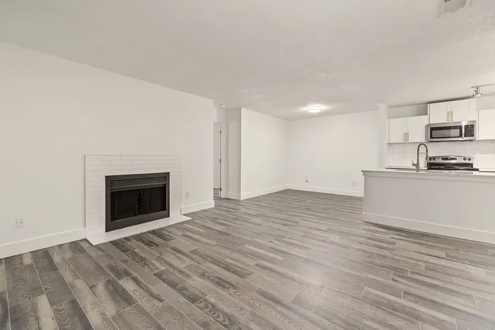Modern open-concept living space featuring elegant hardwood floors, a cozy fireplace, and a sleek kitchen with stainless steel appliances.