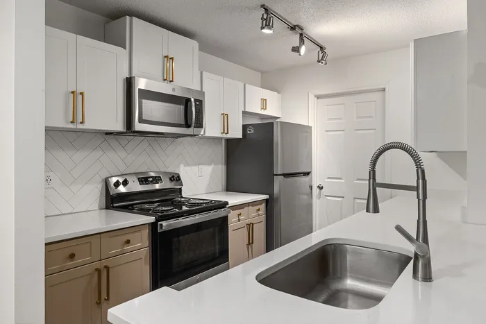 Modern kitchen with sleek stainless steel appliances, stylish herringbone backsplash, and contemporary lighting.