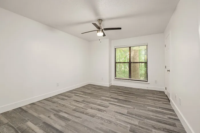 Bright, modern room with chic wood flooring, neutral walls, and a large window overlooking lush greenery.