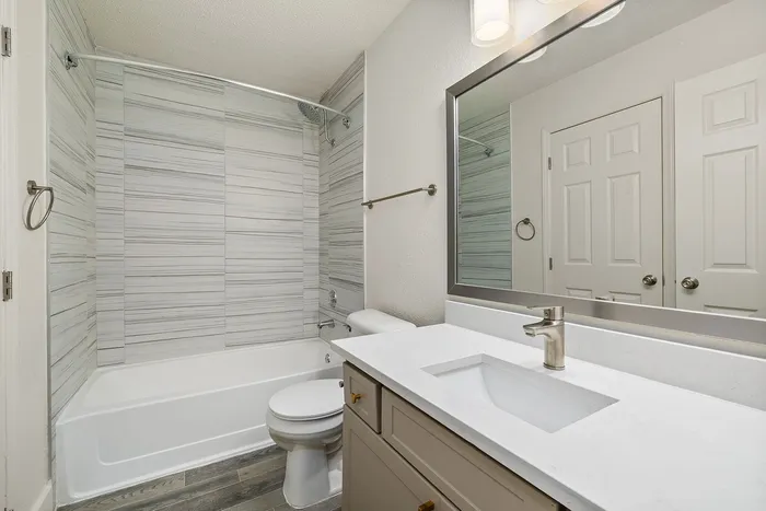 Modern bathroom featuring elegant light wood cabinetry, sleek quartz countertops, and a beautifully tiled shower area.