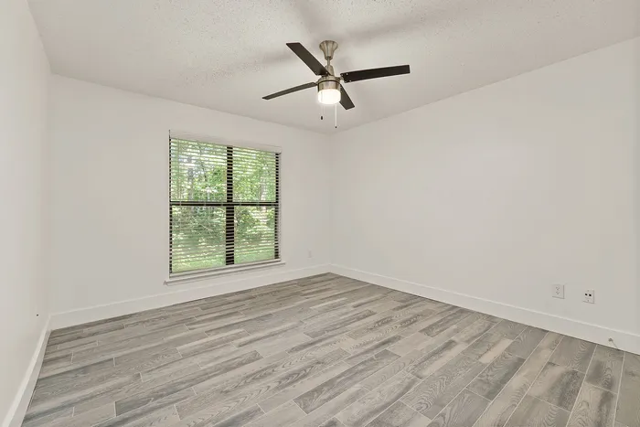 Bright empty room with large window, sleek wooden flooring, and modern ceiling fan, ideal for personal design and decoration.