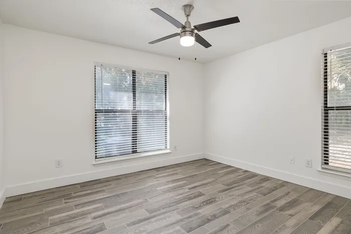 Bright and airy room featuring sleek hardwood floors, modern ceiling fan, and large windows with blinds.