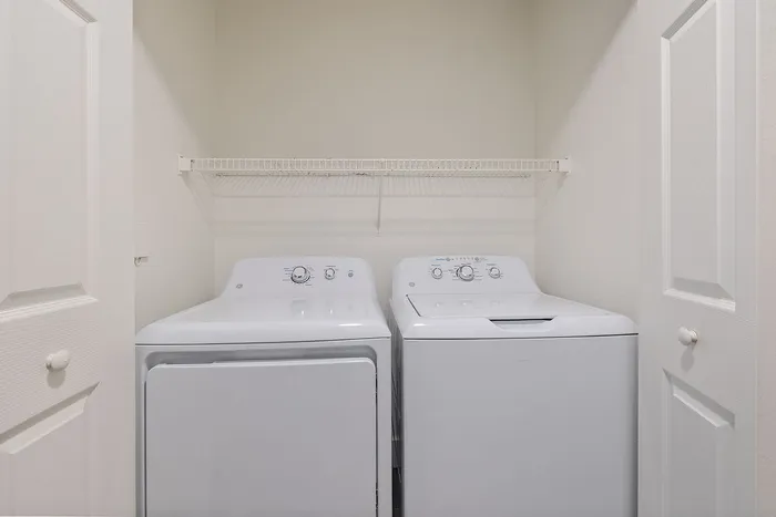 Modern laundry nook featuring a high-efficiency washer and dryer with sleek white design, complemented by a convenient overhead shelf.
