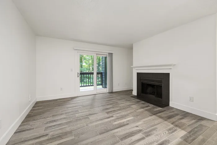 Elegant living room with modern hardwood floors, a cozy fireplace, and large sliding doors opening to a serene balcony view.