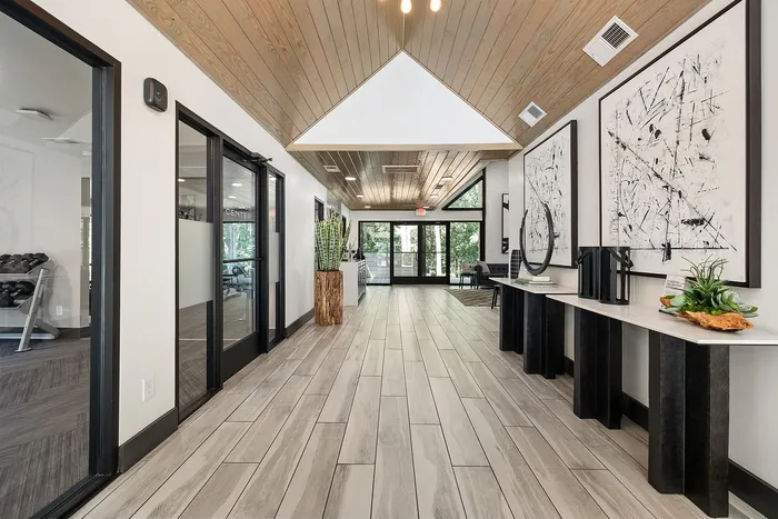 Inviting apartment lobby with elegant wooden ceiling and floor tiles, modern black-and-white artwork, and glass doors for natural light.