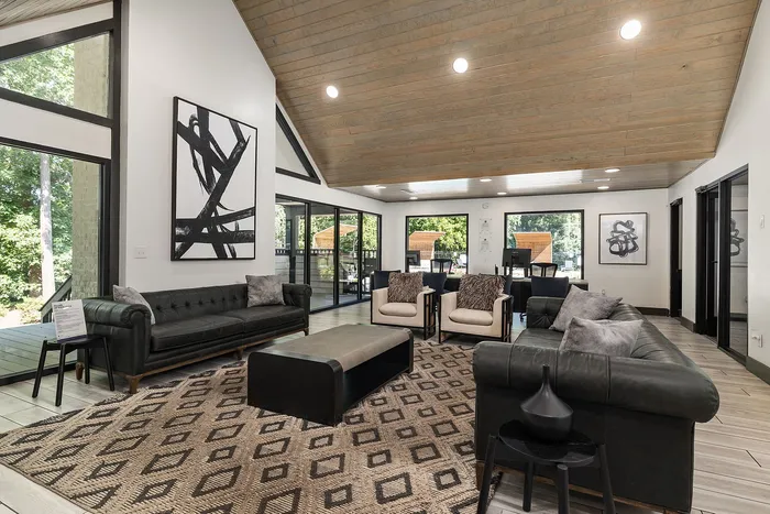 Elegant living room with large windows, modern artwork, stylish black leather sofas, and a cozy seating area overlooking lush greenery.