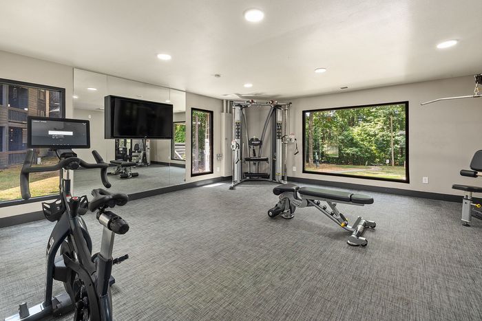 Modern fitness room with state-of-the-art equipment, mirrored walls, and large windows offering a scenic forest view.