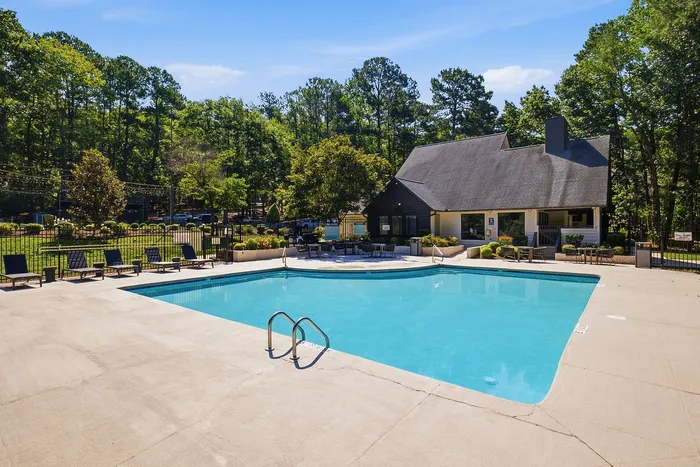 Inviting outdoor pool area surrounded by lush greenery, featuring comfortable lounge chairs and a charming clubhouse.