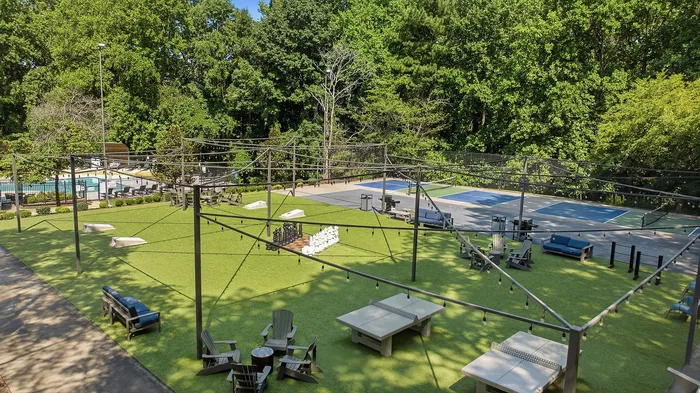 Inviting outdoor recreational area featuring lush green space, tennis courts, a refreshing pool, and cozy seating under string lights.