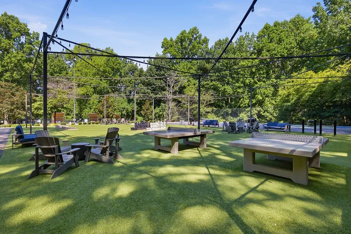 Inviting outdoor recreational area featuring ping pong tables, comfortable seating, and lush greenery under twinkling string lights.