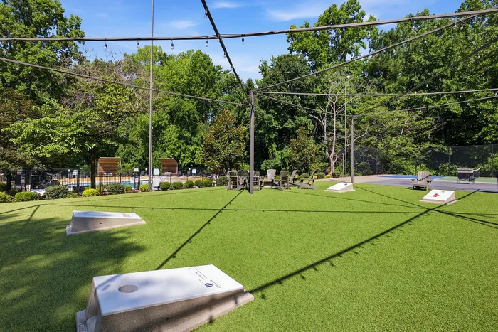 Vibrant outdoor recreation area featuring lush green lawn, cornhole game setup, cozy seating, and surrounded by serene trees.