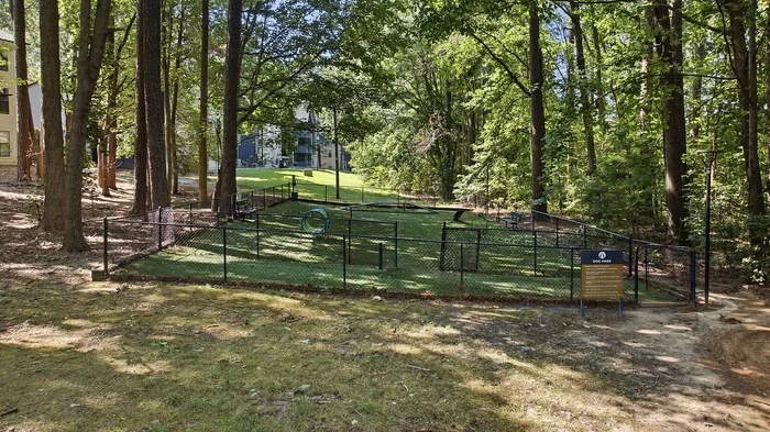 Charming fenced dog park nestled in a lush wooded area, perfect for pet owners seeking a peaceful and natural setting.