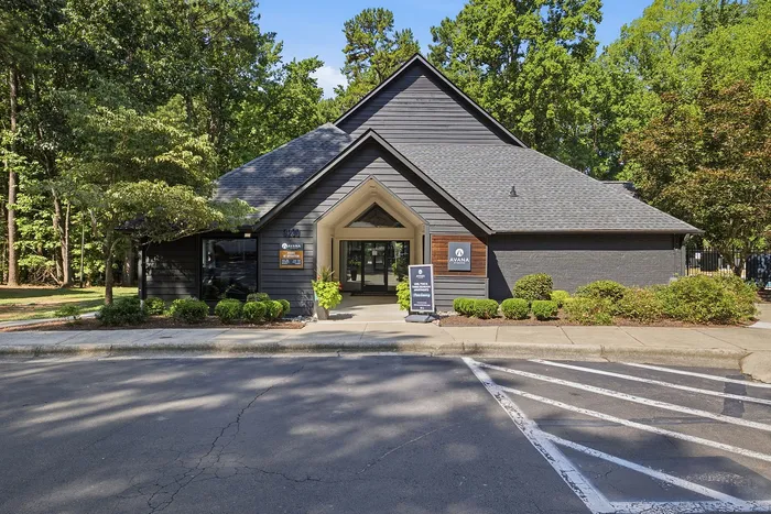 Charming apartment leasing office surrounded by lush greenery, featuring modern architecture and inviting entrance.