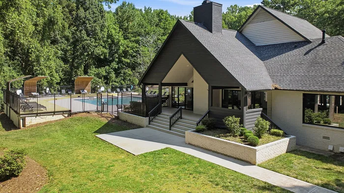Charming clubhouse with modern design surrounded by lush greenery, featuring an inviting pool area with cozy lounge chairs.