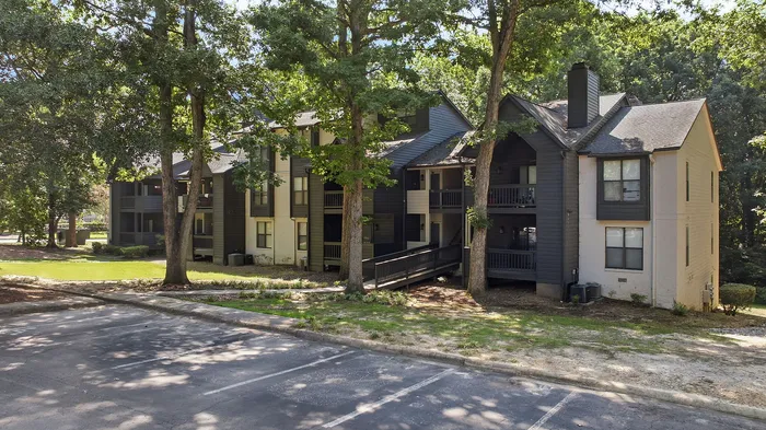Charming apartment complex nestled among lush greenery, featuring a modern exterior and shaded walkways.