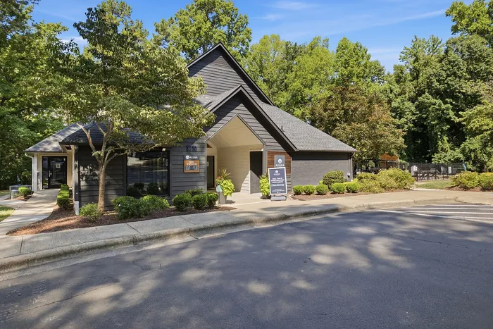 Charming apartment complex with modern architecture nestled among lush greenery, featuring well-maintained landscaping and a welcoming entrance.