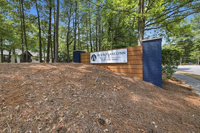 Welcoming entrance to Avana Lake Lynn apartment homes surrounded by lush, green trees and a serene natural setting.