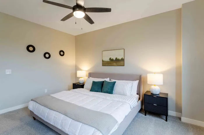 Cozy bedroom featuring a plush king-sized bed with elegant linens, stylish nightstands, and ambient lighting under a modern ceiling fan.
