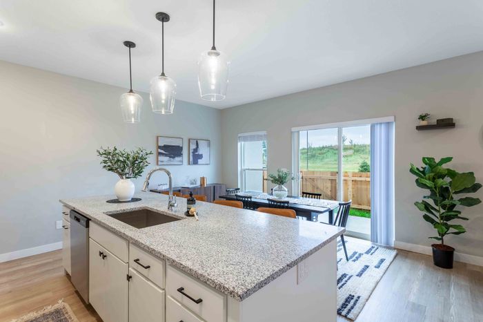 Modern open-concept kitchen and dining area with elegant pendant lighting, spacious island, and large sliding glass doors leading to a lush outdoor view.