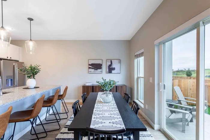 Contemporary dining area with elegant decor, featuring a granite kitchen island, stylish pendant lights, and a view of the lush outdoor patio.