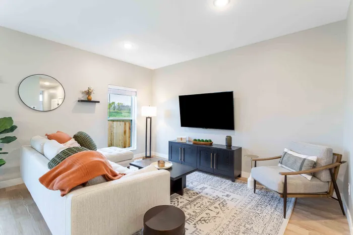 Bright and inviting living room with a cozy sofa, stylish accent chair, modern decor, and large flat-screen TV, ideal for relaxation and entertainment.