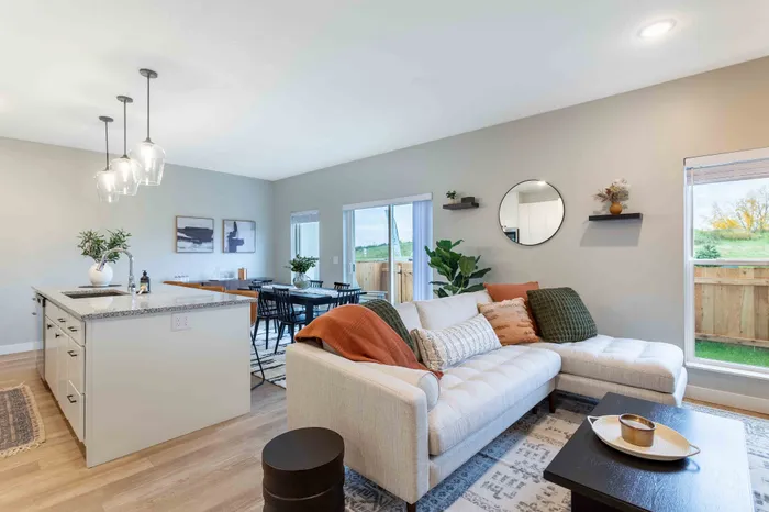 Modern living space featuring a cozy sectional sofa with elegant cushions, a sleek kitchen island with pendant lighting, and a spacious dining area opening to a scenic view.