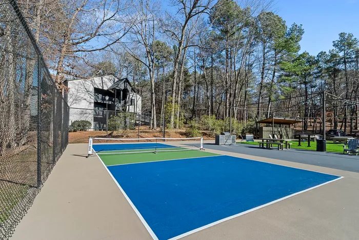 Modern apartment complex with vibrant tennis court surrounded by lush greenery and recreational amenities.