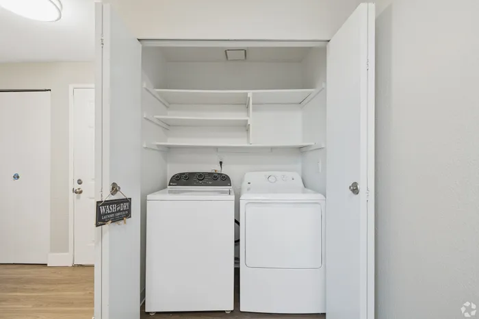 Modern in-unit laundry area with washer and dryer, featuring ample shelving for convenient storage.