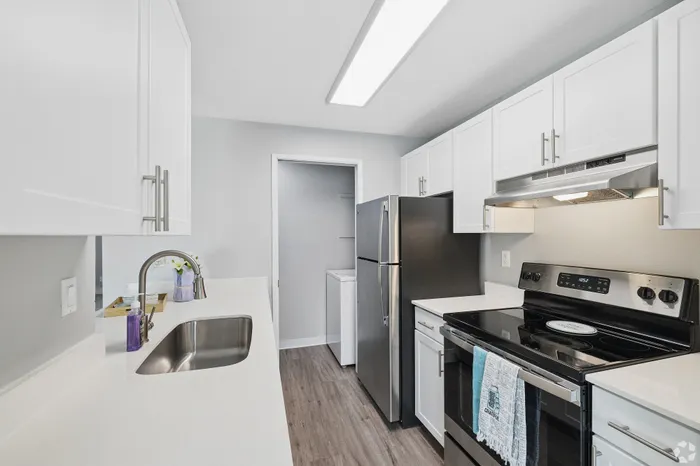 Modern kitchen with sleek stainless steel appliances, pristine white cabinetry, and chic wood flooring creates a bright and inviting cooking space.