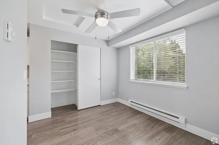 Bright and airy bedroom with modern ceiling fan, large window, and sleek built-in closet shelving.