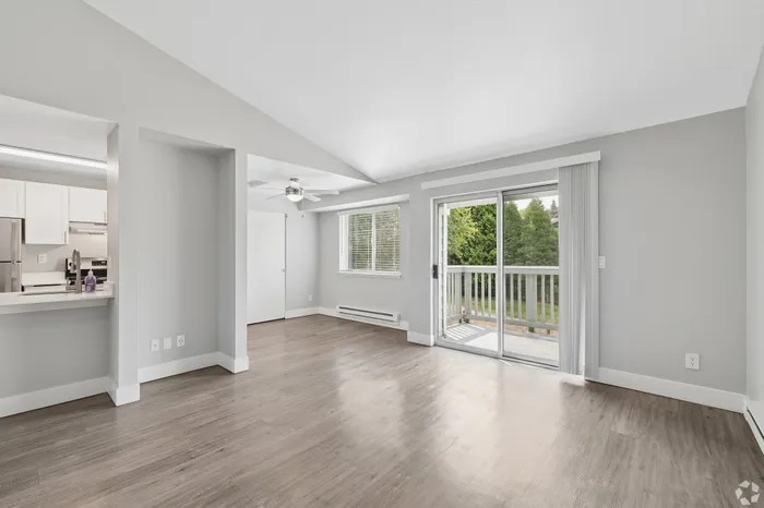 Bright and spacious living area with modern laminate flooring, adjacent kitchen, and sliding doors opening to a scenic balcony view.