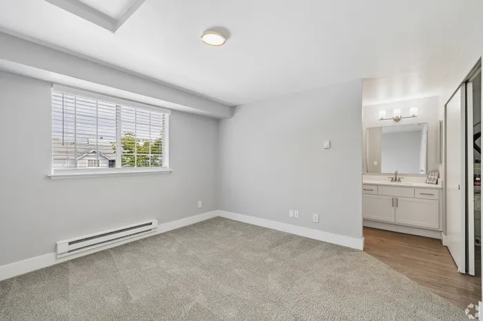 Bright bedroom with plush carpeting, large window with blinds, and an elegant ensuite bathroom.