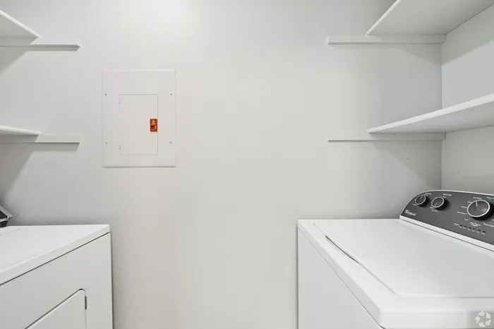 Modern utility room featuring sleek white washer and dryer units with built-in shelving for ample storage.