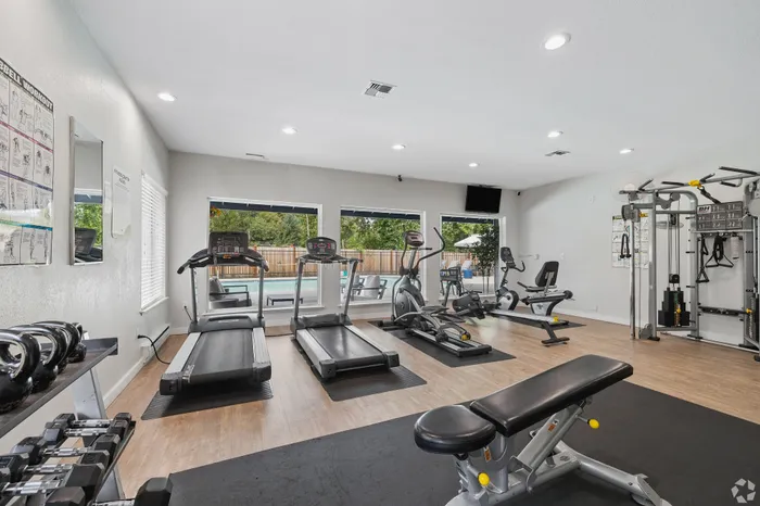 Modern fitness center with treadmills, weight machines, and a view of the outdoor pool, offering a bright and inviting workout space.