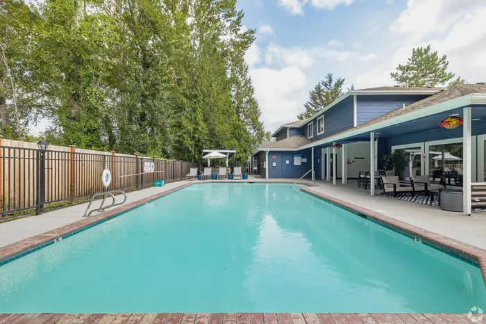 Inviting outdoor swimming pool with sun loungers, surrounded by lush trees and a stylish clubhouse, perfect for relaxation and social gatherings.