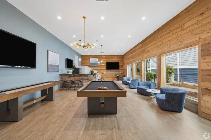 Modern entertainment room featuring a pool table, chic blue armchairs, and stylish wood paneling with ample natural light.