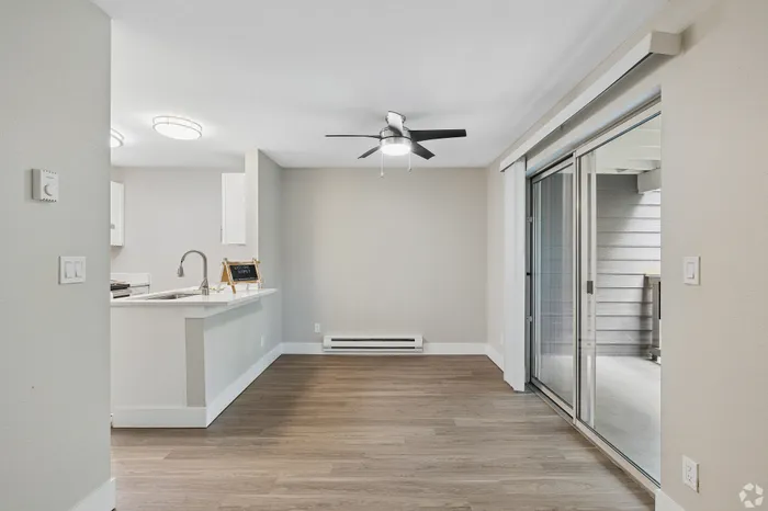 Modern apartment space featuring sleek wood flooring, a stylish white kitchen with an island, and large sliding glass doors opening to a private balcony.
